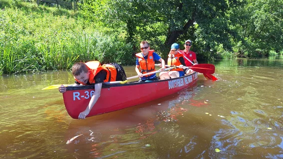 4 Jungs im Kanu, fleißig am Rudern. Der Erste im Boot möchte einen Fisch fangen.